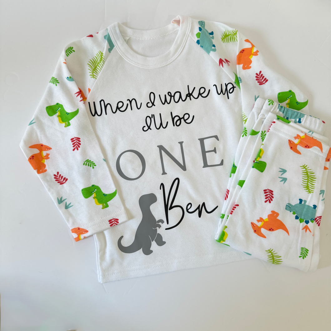 Children's pyjamas, white long sleeved with dinosaur printed arms. Pyjama bottoms with dinosaur print
